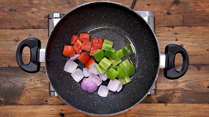 Onion cubes, capsicum and tomato cubes added in hot oil in pan.