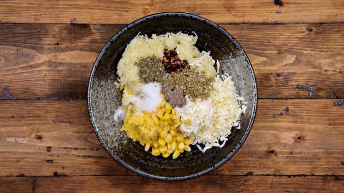 Ground corn, boiled potato, grated cheese, corn kernels, chili flakes, herbs, salt and pepper added in bowl.
