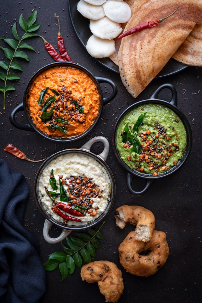 3 different types of South Indian coconut chutney (red, white, green) served in 3 different black bowls.