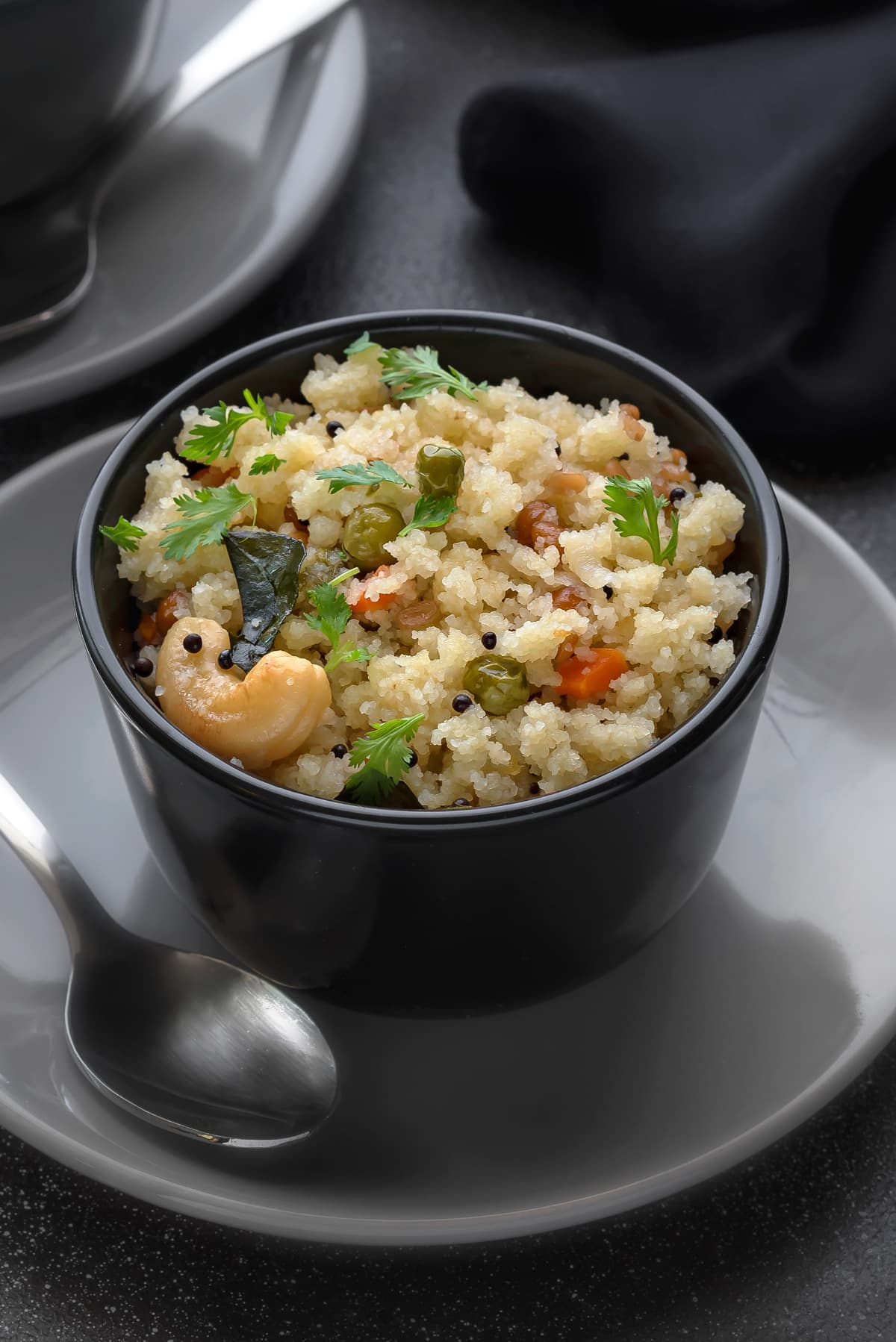 Close-up shot of South Indian rava upma that is served in black bowl, spoon on side.