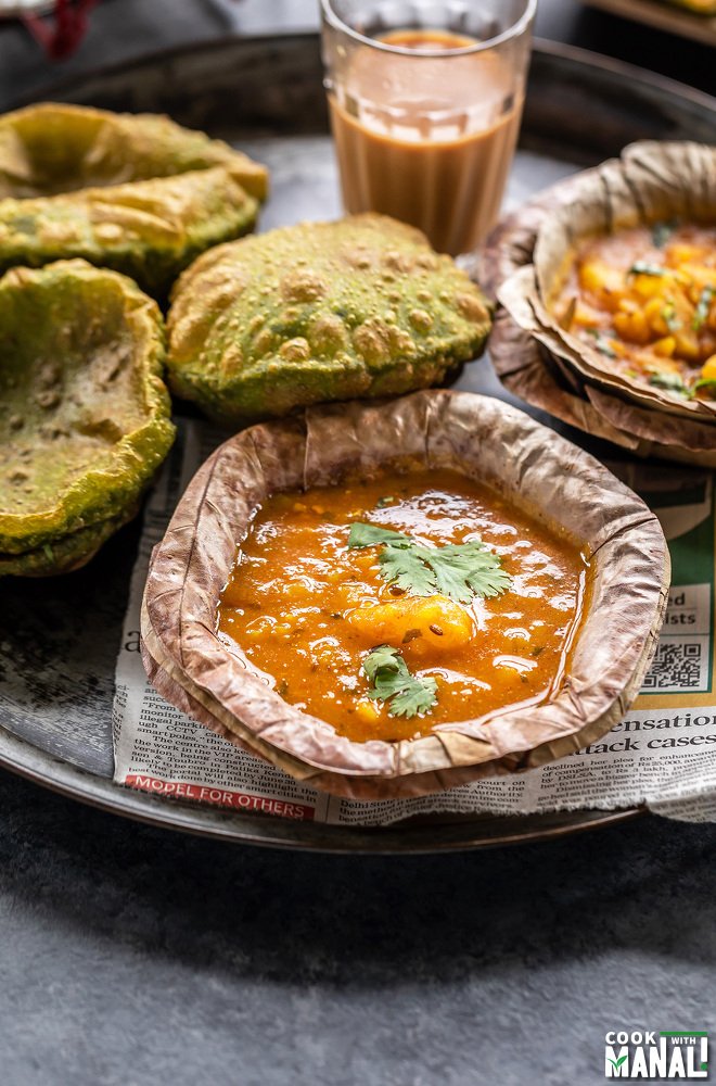potato curry served in a traditional Indian leaf bowl and puris and chai placed in background