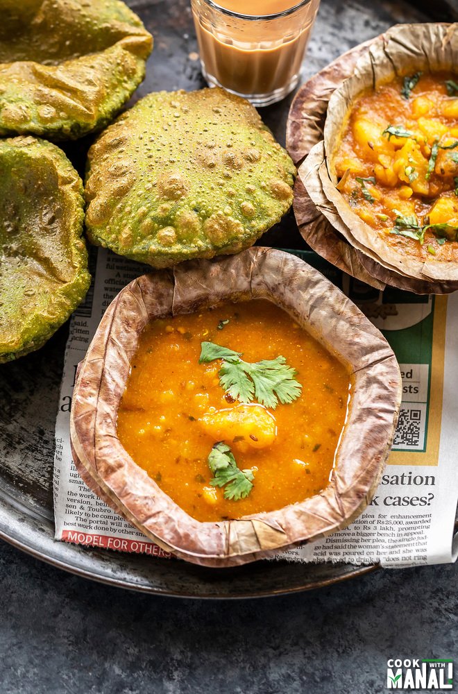 potato curry served in a traditional Indian leaf bowl and puris and chai placed in background