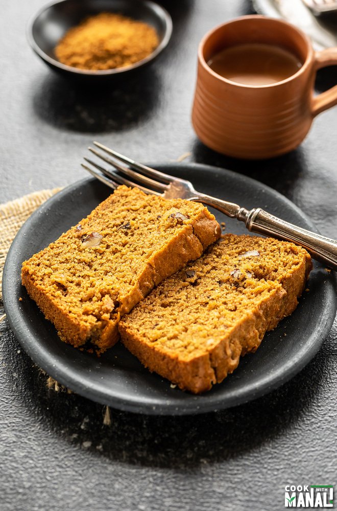 two slices of whole wheat jaggery cake in a plate with a cup of chai in the background