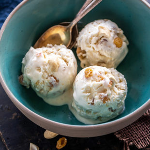 3 scoops of white color ice cream served in a blue bowl with 2 golden spoons placed on the side