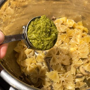 pesto in a measuring cup being added to a pot of pasta