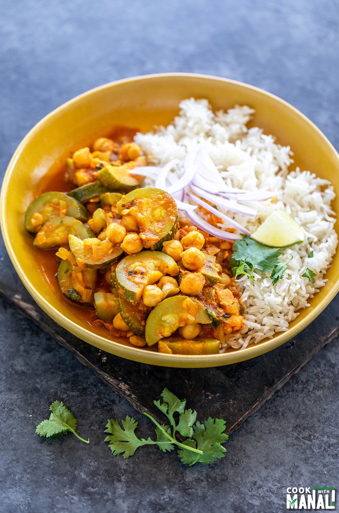 zucchini chickpea curry served with white rice in a yellow color bowl topped with sliced onion, cilantro and a lime wedge