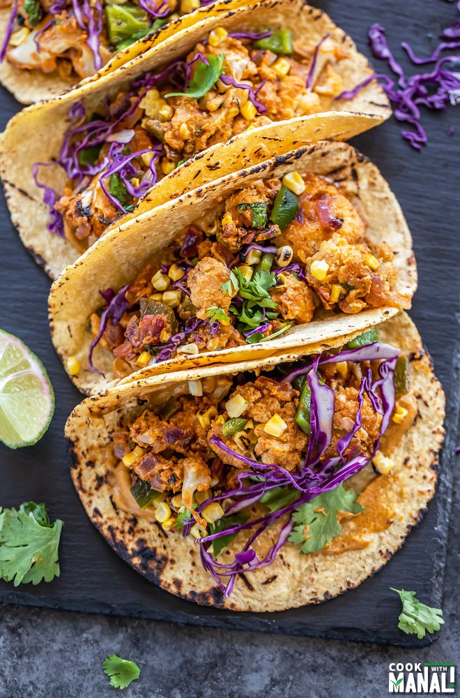 3 tacos filled with cauliflower, topped with cilantro and arranged on a black board
