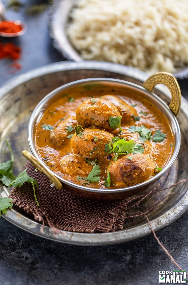 dum aloo served in a copper kadai garnished with cilantro with a plate of rice in the background